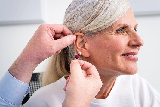 Ältere Frau bekommt ein modernes Hörgerät ins Ohr eingesetzt, Hörhilfe Beratung.